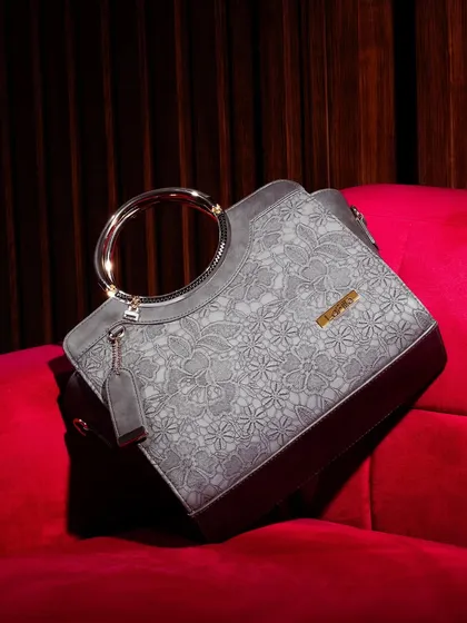 A luxury handbag with a unique floral texture and a metallic ring handle, placed on a rich, red velvet couch. This setting screams opulence and positions the product as a high-end statement piece.