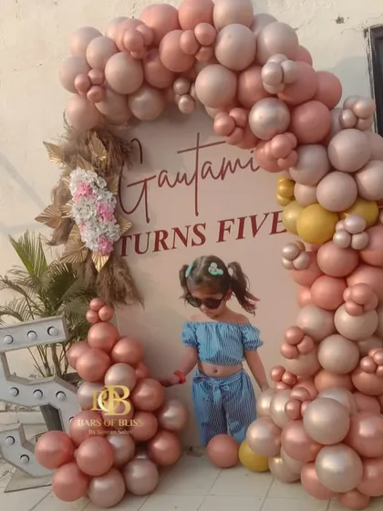 An adorable setup for a 5th birthday party. The personalized backdrop features a photo of the birthday girl, framed by a beautiful arch of pastel pink and rose gold balloons.