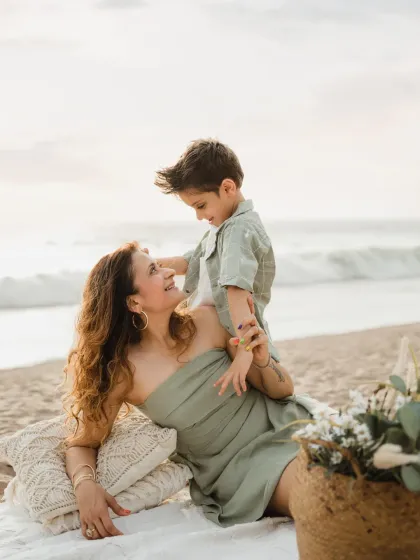 A mother and son share a sweet look during their family beach photoshoot. The boho-chic picnic setup adds a stylish touch.