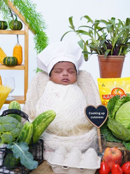 Cooking up cuteness. This tiny chef theme is absolutely adorable. The baby is wrapped in white with a chef's hat, surrounded by fresh vegetables and kitchen props.