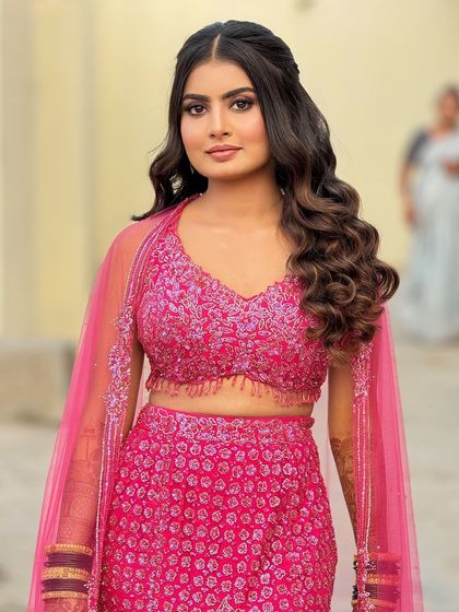 A full-length shot of the bride in her pink reception lehenga, her hair styled in beautiful, soft waves.