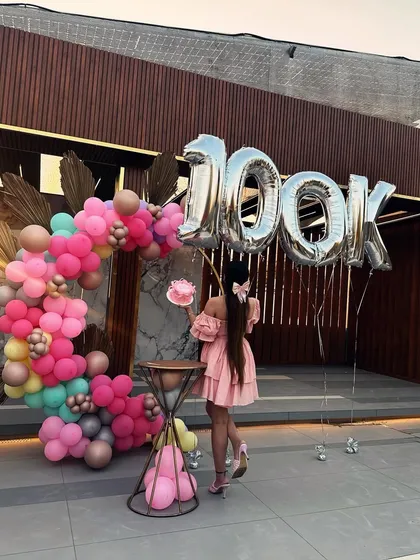 A behind-the-scenes look at the 100k celebration setup, featuring a colorful balloon arch and large '100K' foil balloons.
