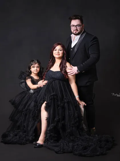 A powerful and glamorous family maternity portrait. The all-black, formal attire against a simple dark background creates a very striking and elegant image.