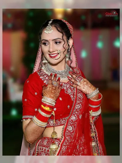 A classic bridal portrait showcasing the bride's radiant smile. Her traditional red lehenga, elaborate jewelry, and detailed henna are beautifully captured against a softly lit event background.
