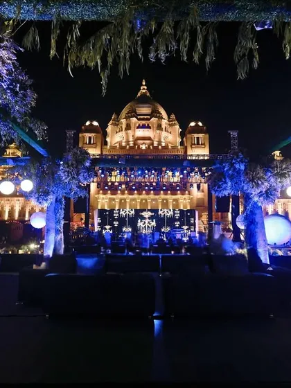 A captivating view of the lounge setup, with the neon-lit trees framing the magnificent Umaid Bhawan Palace in the background, blending modern design with royal architecture.