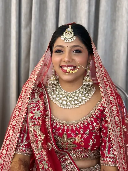 A radiant smile on a classic North Indian bride. I created this look with soft, glowing skin and a bold red lip to perfectly complement her stunning red lehenga for the main wedding ceremony.
