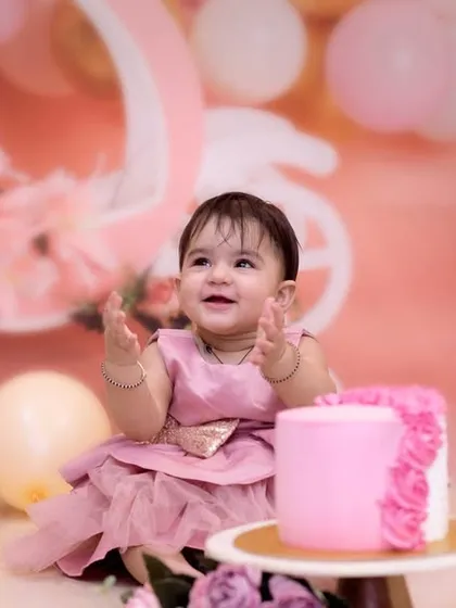 The moment of anticipation right before the cake smash begins. This little girl is all smiles, surrounded by a beautiful pink and gold setup for her first birthday.