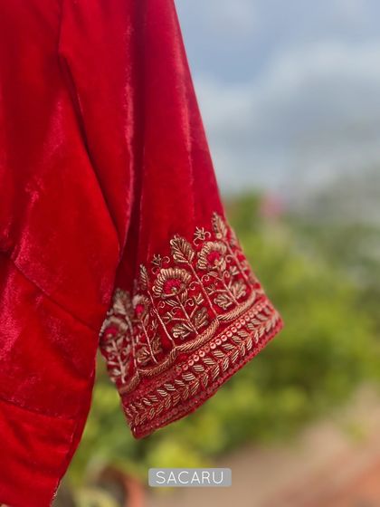 A close-up of the intricate zardosi embroidery on the sleeve cuff of the bright red velvet blouse, showcasing the detailed craftsmanship.
