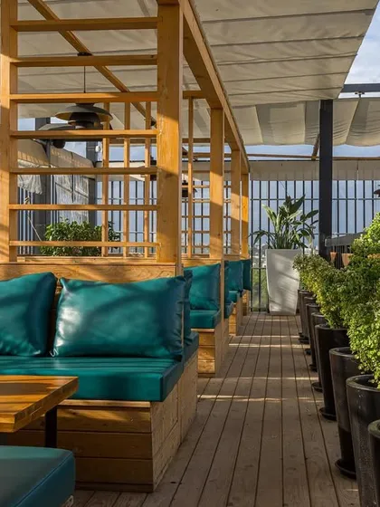 The rooftop terrace seating, with its wooden pergola and lush planters, offers a breezy and relaxing atmosphere. The design is meant to feel like an escape, high above the city streets.