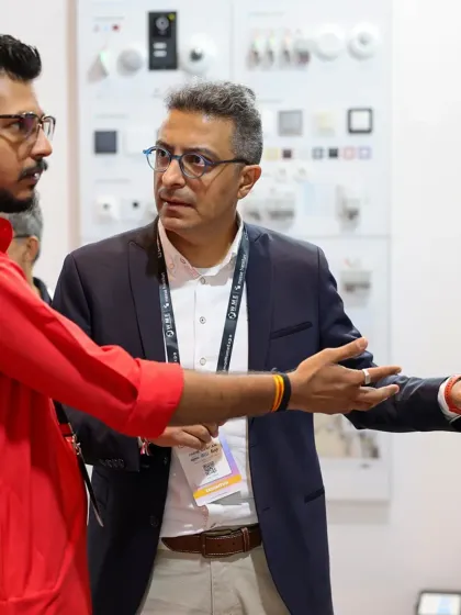 An exhibitor points out the features of a wall-mounted control panel to a professional visitor, highlighting the importance of direct interaction and expert guidance.