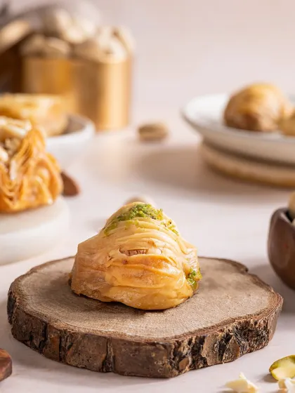 A close-up of a delicate, flaky baklava. I used a rustic wooden slice as a prop to contrast with the dessert's refined layers, highlighting its texture.