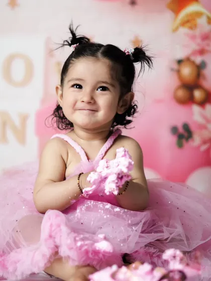 A happy, messy smile with pink frosting on her hands. This is the classic cake smash moment that every parent loves to see.