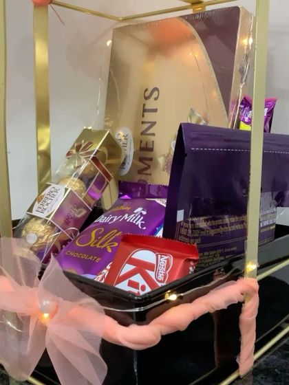 Another view of the chocolate-filled metal bow hamper, highlighting the layers of different treats like Ferrero Rocher, Dairy Milk Silk, and KitKat.