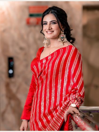 A radiant portrait of the bride, Vanaja. Her bright red and gold saree pops against the simple background, and her joyful smile lights up the frame.