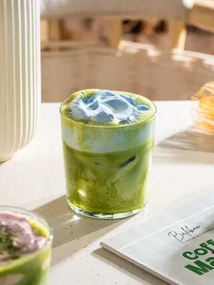 An iced matcha with a creative blue pea flower foam on top. The color combination is stunning.