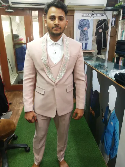 This client is seen during a fitting for his three-piece suit in a distinctive light pink fabric. The design includes detailed embroidery on the waistcoat and lapels, showcasing our ability to create unique, personalized groomswear.