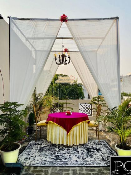 An elegant and romantic cabana setup for two on a terrace, perfect for a daytime surprise. The white drapes, classic chandelier, and vibrant pink tablecloth create a beautiful private dining experience.