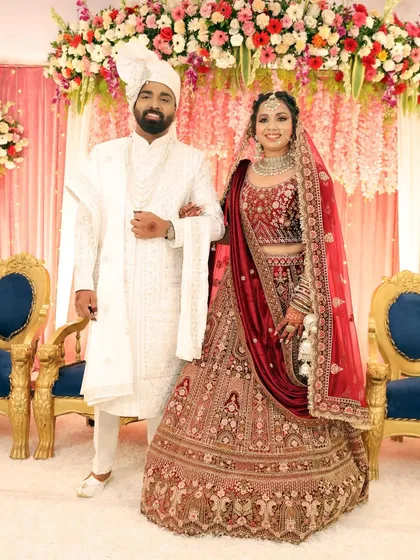 The happy couple posing on their wedding day. The bride's classic red lehenga is paired with timeless makeup for an elegant and beautiful look.