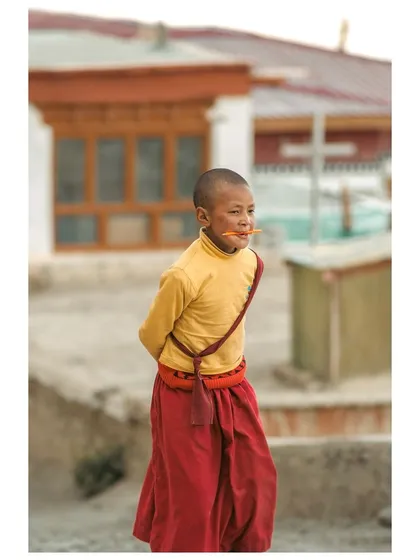A young monk with a playful expression, his face smeared with something orange, captured in a candid moment.