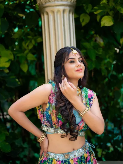 A close-up portrait of a model ready for a Mehendi ceremony. The focus is on her intricate makeup, jewelry, and the vibrant colors of her festive attire.