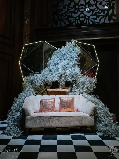 A unique photo-op area featuring a geometric, mirror-panelled heart structure overflowing with baby's breath. The checkered floor and blush sofa completed this modern and artistic corner.