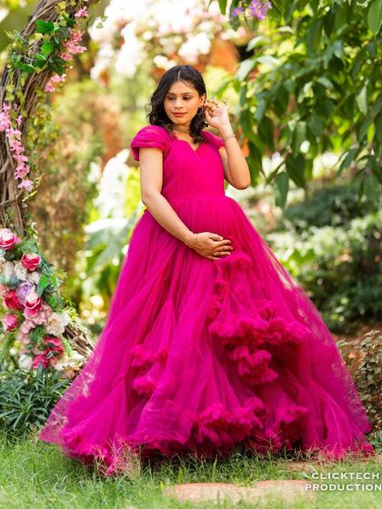 A solo maternity portrait with a flowing pink gown in front of a rustic floral arch.