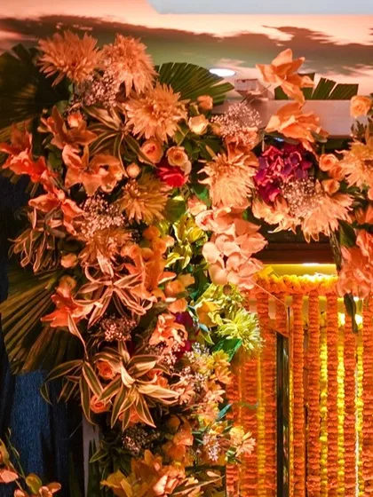 A lush floral arrangement framing a doorway, with a curtain of marigolds in the background. The mix of different flowers and foliage creates a rich and abundant look.