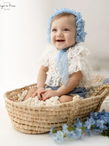 A bright and joyful portrait of a baby girl in a basket, surrounded by blue flowers.