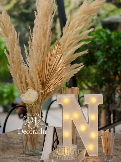The magic is in the details. This elegant table centerpiece for a 40th birthday combines natural pampas grass with a single white rose and a gilded palm leaf, showcasing our flair for boho-chic arrangements.