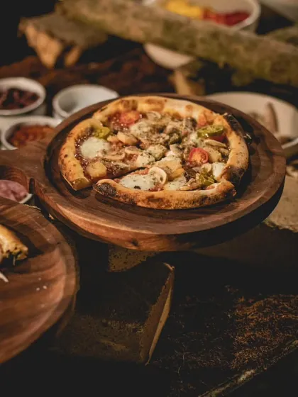 A gourmet vegetarian pizza is presented on a rustic wooden platter. Topped with artisanal cheese and fresh vegetables, our sourdough pizzas are a highlight of our global cuisine offerings.