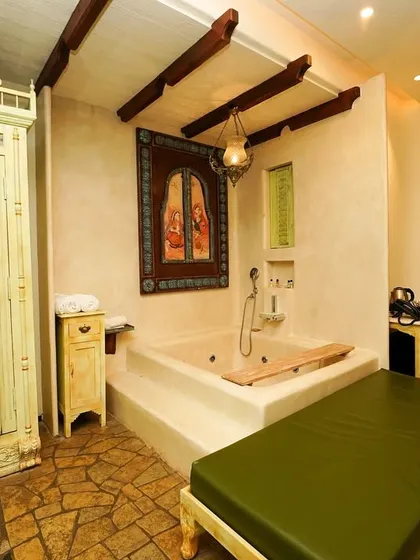 A view of the suite's spa area, featuring a built-in bathtub, a vintage-style wardrobe, and unique architectural details like exposed wooden beams.