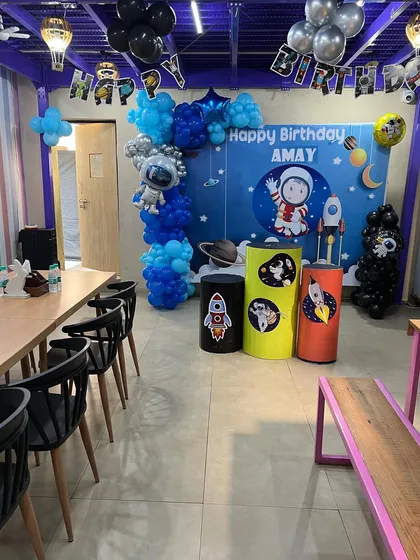 The indoor setup for our space party, with a personalized backdrop, planet-themed plinths, and an astronaut balloon sculpture.