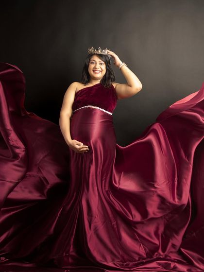 A regal portrait of a mom-to-be adjusting her crown. The rich, flowing fabric of the wine-red gown makes her look and feel like a true queen.
