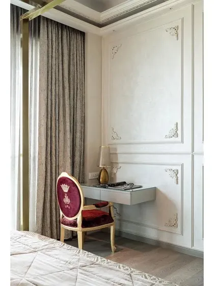 The queen's desk, a chic vanity area set against the detailed wall paneling. The elegant chair with its wine-colored upholstery and crown detail adds a touch of royalty to this personal corner.