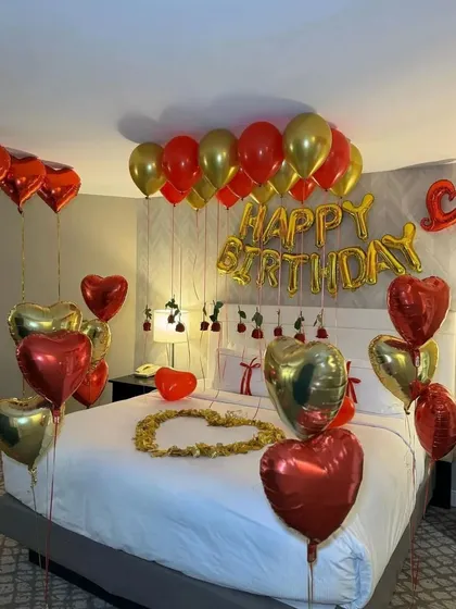 A full view of the red and gold romantic birthday setup, with 'Happy Birthday' foil letters above the bed.