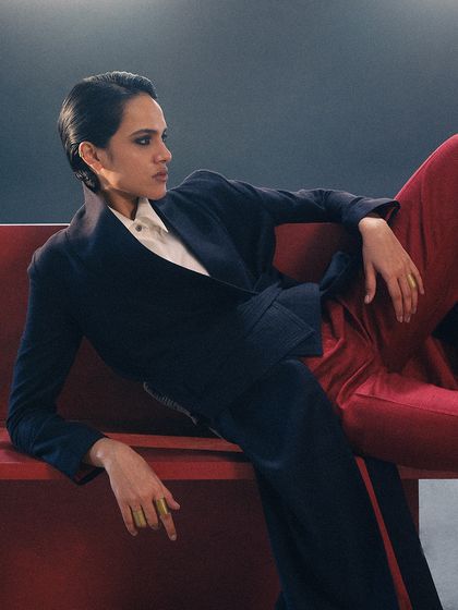 The model reclines on a red architectural element, creating a strong diagonal line. The color palette of red, navy, and white is a consistent theme in this campaign.