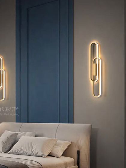 A pair of modern interlocking loop wall sconces in a bedroom. These fixtures provide a soft, indirect glow, perfect for creating a relaxing atmosphere.