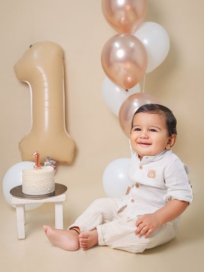 A classic first birthday portrait with a simple cake and balloons. The neutral, earthy tones create a calm and timeless look for this milestone session.