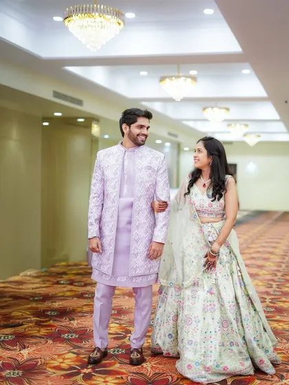A full-length portrait of the couple walking through the venue during their engagement shoot. Their coordinated pastel outfits look beautiful against the modern architecture of the hall.