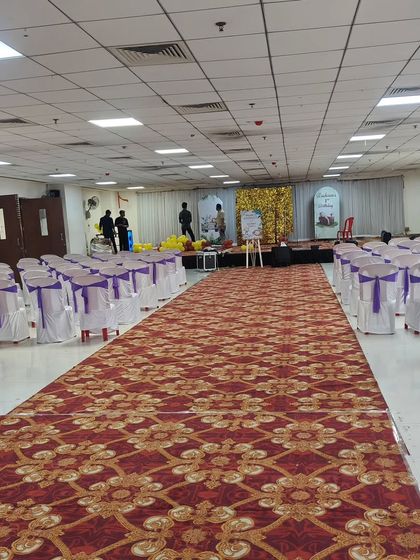 The hall setup for a first birthday party. The aisle is clear, and the chairs are arranged with purple sashes, leading to the decorated stage.