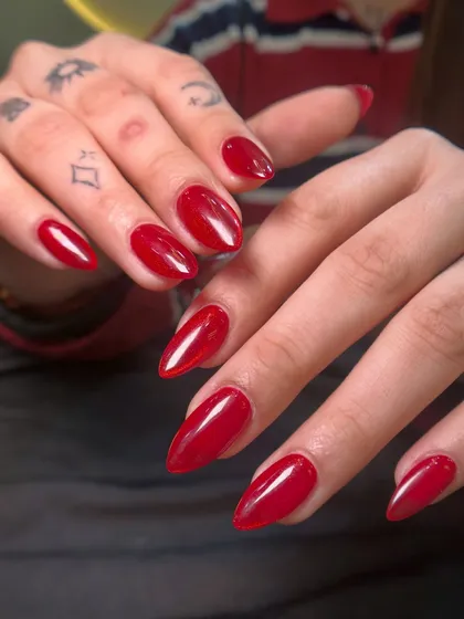 This vibrant red manicure is a statement in itself, perfectly complementing the client's edgy finger tattoos.