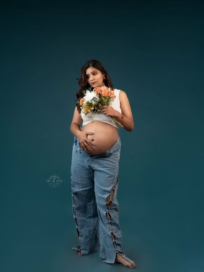 A modern and edgy maternity portrait of a mom-to-be in ripped jeans and a crop top, holding a bouquet of flowers.