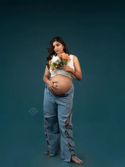 A modern and edgy maternity portrait of a mom-to-be in ripped jeans and a crop top, holding a bouquet of flowers.
