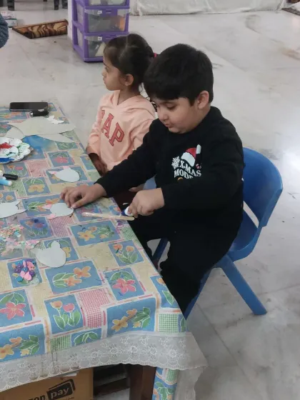 A child carefully works on his craft project at the table. The setup with various art supplies encourages children to make their own creative choices.