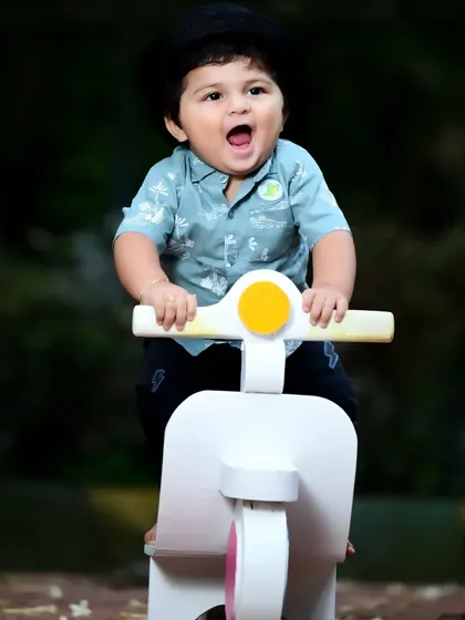 A happy baby boy enjoying a ride on his toy scooter in a park setting.