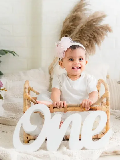 A happy birthday girl in her beautiful white dress. This simple and sweet setup lets her joyful personality shine through on her first birthday.