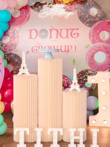 A sweet 'Donut Grow Up' theme for a first birthday. This playful setup includes giant donut and cupcake props, a custom backdrop, and a light-up number '1' in a fun and colorful arrangement.