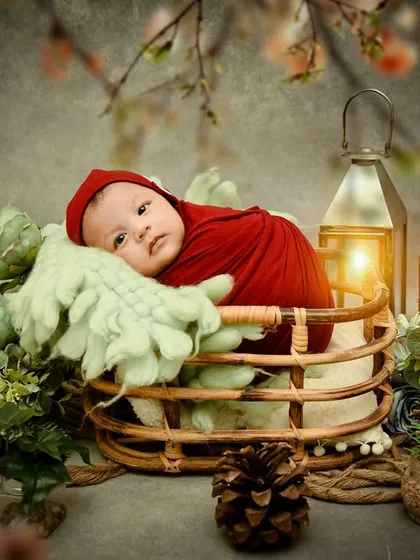 An awake newborn with a curious expression, wrapped in red and nestled in a basket. This enchanted forest theme is great for capturing those special wide-eyed moments.