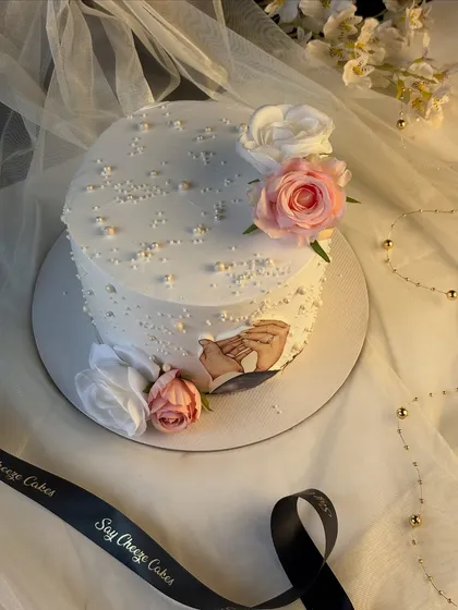 An overhead view of the 25th-anniversary cake, showing the arrangement of the floral decorations and the custom edible image. The design is set against a delicate, sheer fabric backdrop, emphasizing its elegance.