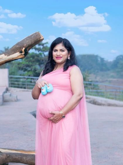 A lovely outdoor portrait holding tiny blue baby shoes. The bright blue sky and the soft pink of her gown create a beautiful color palette for this announcement.